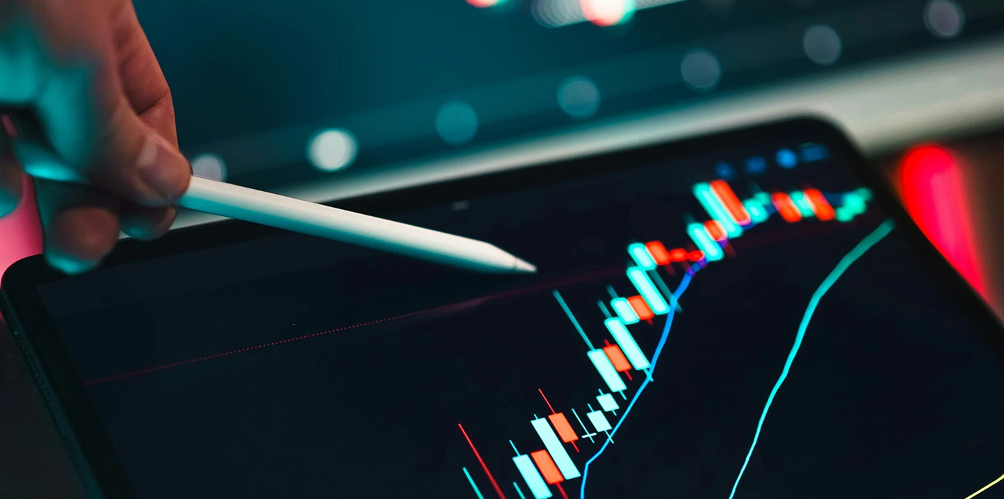 Mano utilizando un lápiz digital sobre una tableta que muestra un gráfico financiero en ascenso.