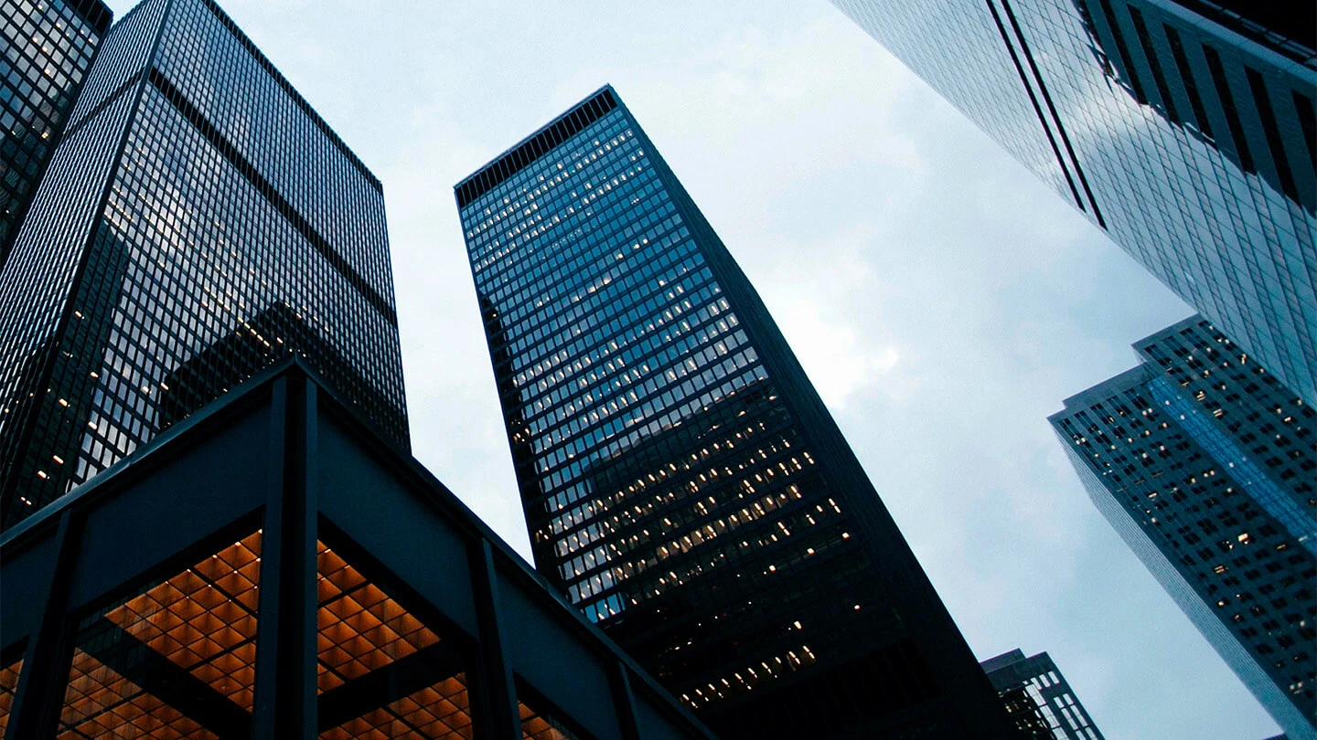 Vista desde abajo de varios rascacielos con fachadas de vidrio y acero iluminadas.
